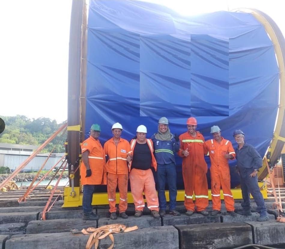 Equipe de rigging reunida junto à carga amarrada sobre berço de madeira em operação de movimentação portuária